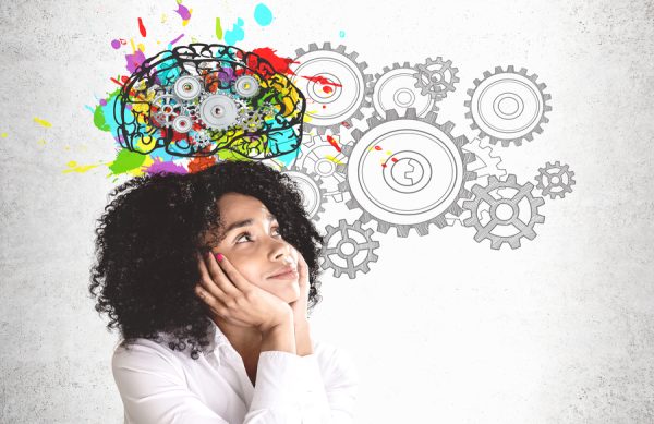 Smiling young African American woman in white shirt looking at colorful brain sketch with gears drawn on concrete wall. Concept of brainstorming